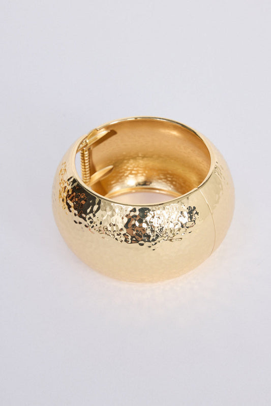 Model wearing Maura Bangle in gold with snap lock closure and hinge for easy wear, lifestyle wrist view on neutral background