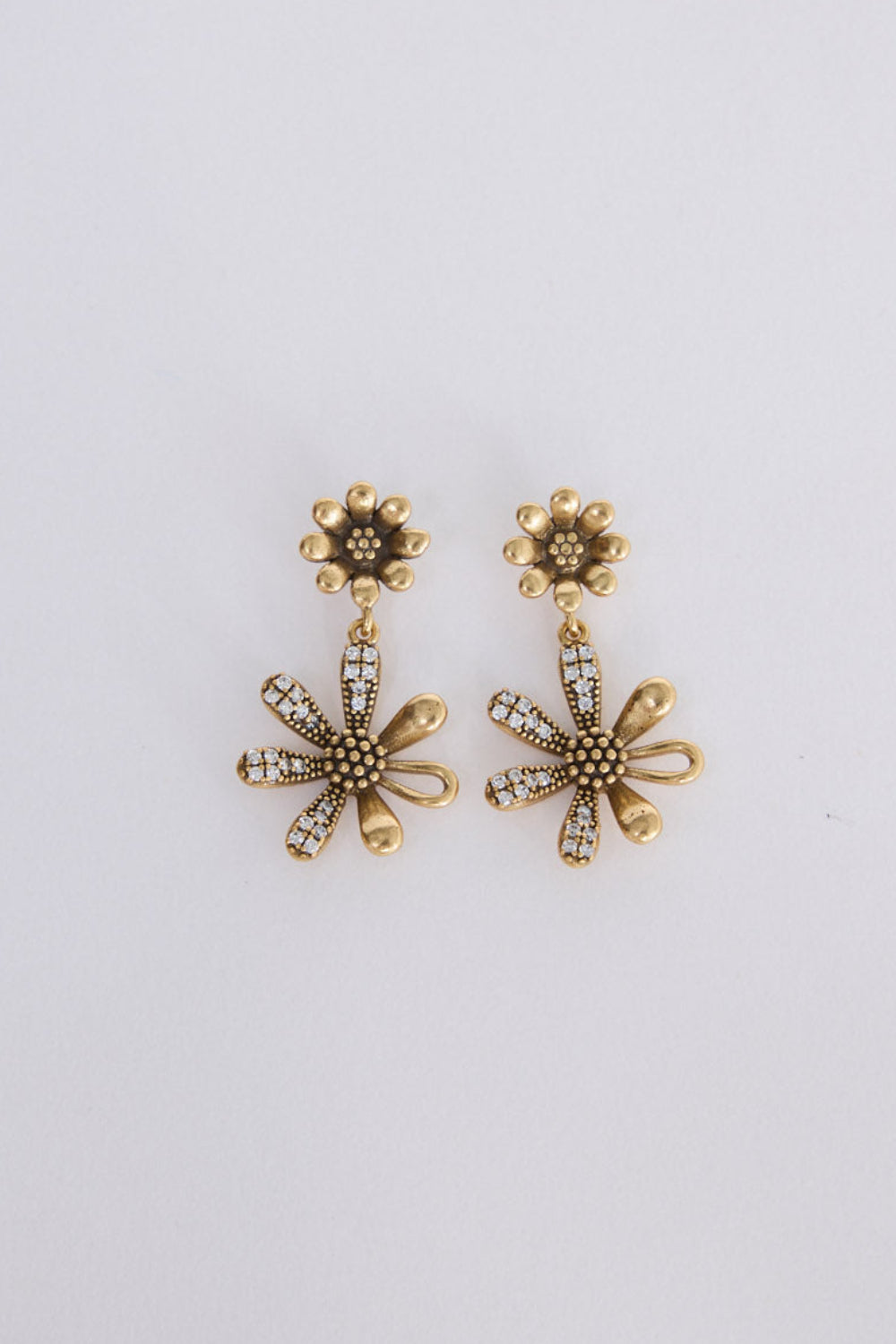 A pair of gold-toned flower-shaped drop earrings with textured centers and small clear rhinestone accents, displayed on a plain light gray background.