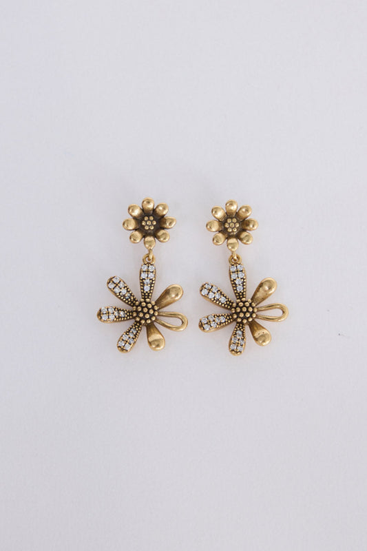 A pair of gold-toned flower-shaped drop earrings with textured centers and small clear rhinestone accents, displayed on a plain light gray background.