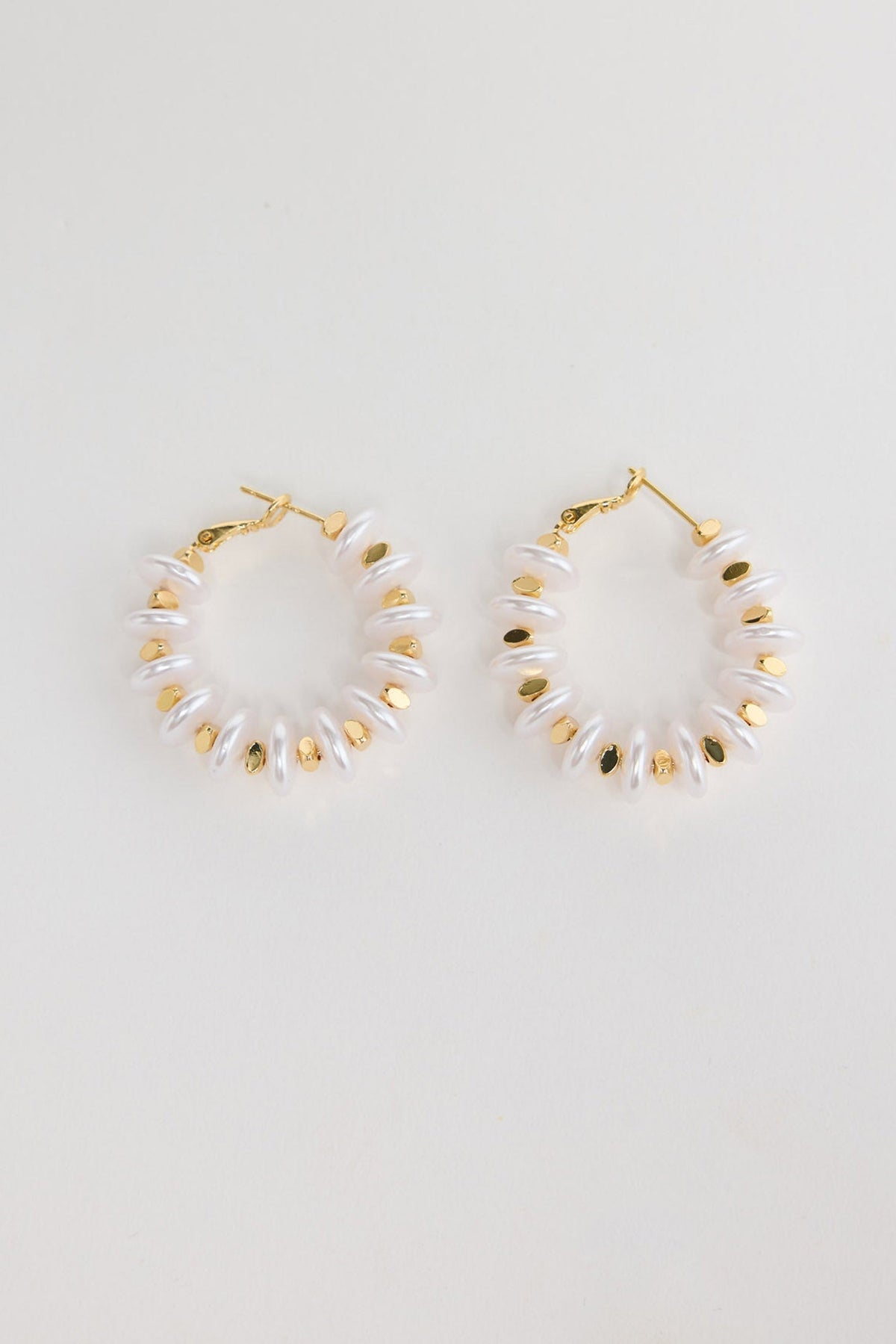 Pair of gold-tone hoop earrings made of stacked white pearl-look rondelle beads with small gold accents, laid flat on a white background