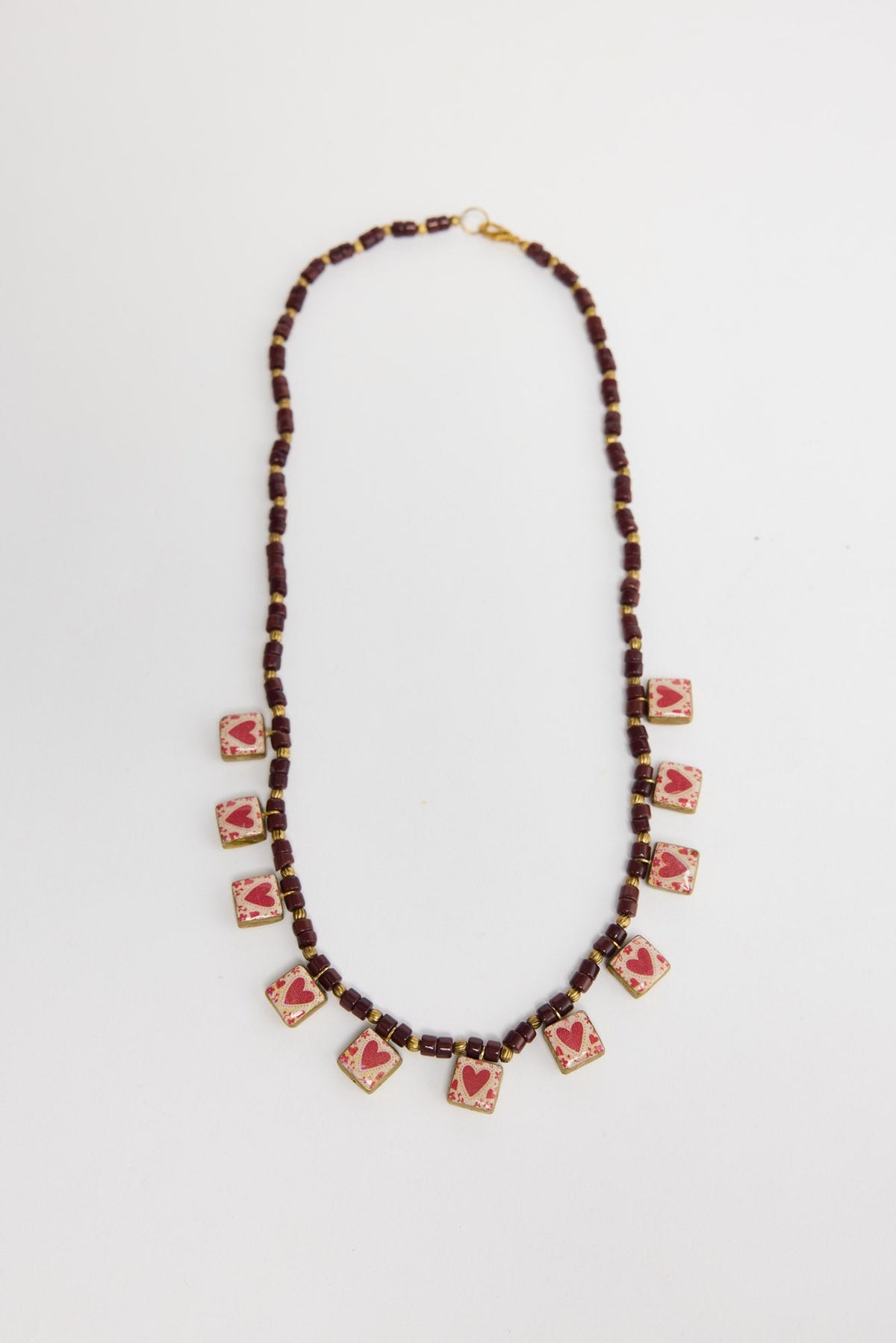 Love Sick beaded necklace in Red laid flat, showing the burgundy bead strand with a row of heart-print square charms