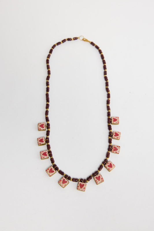 Love Sick beaded necklace in Red laid flat, showing the burgundy bead strand with a row of heart-print square charms