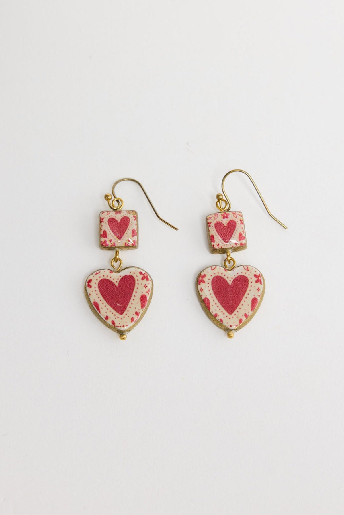 Pair of Love Sick drop earrings in Red laid flat, showing the square heart-print charm and heart-shaped drop