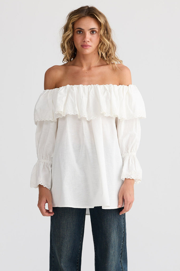 Woman wearing a white off-shoulder top and dark jeans on a white background