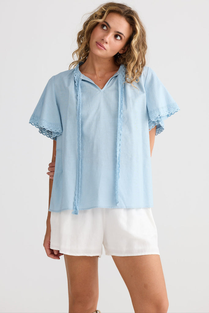 Woman wearing a light blue blouse and white shorts on a plain background