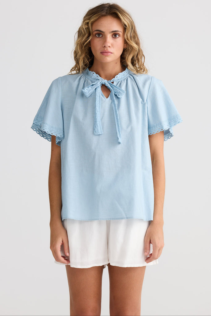Woman wearing a light blue blouse with ruffled sleeves on a white background