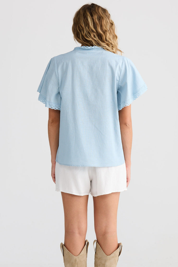 Woman wearing a light blue shirt, white shorts, and tan boots on a white background