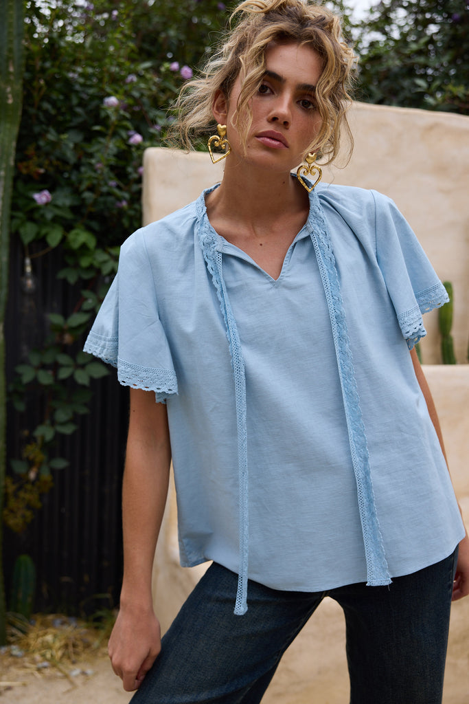 Woman wearing a light blue blouse with ruffled sleeves outdoors.