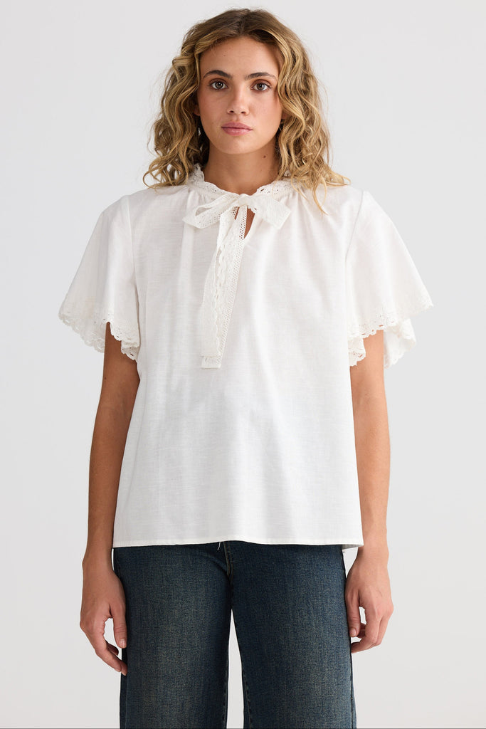 Woman wearing a white blouse with ruffled sleeves on a plain background