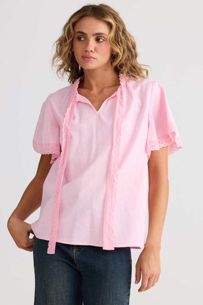 Woman wearing a light pink blouse with short sleeves and a tie detail on a white background