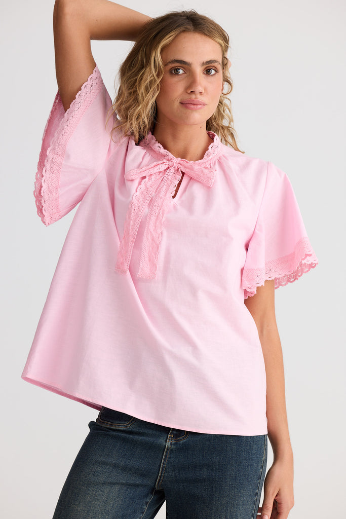 Woman wearing a pink blouse with ruffled sleeves and a bow tie on a white background
