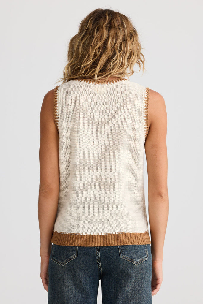 Person wearing a cream sleeveless top with brown trim on a plain background