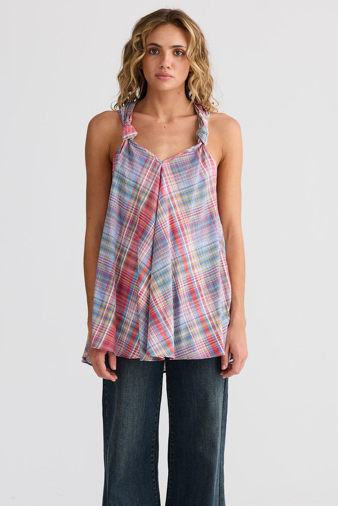 Woman wearing a plaid sleeveless top and wide-leg jeans on a white background