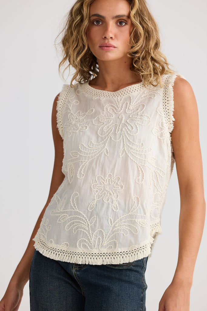 Woman wearing a white top with embroidered detail against a plain background