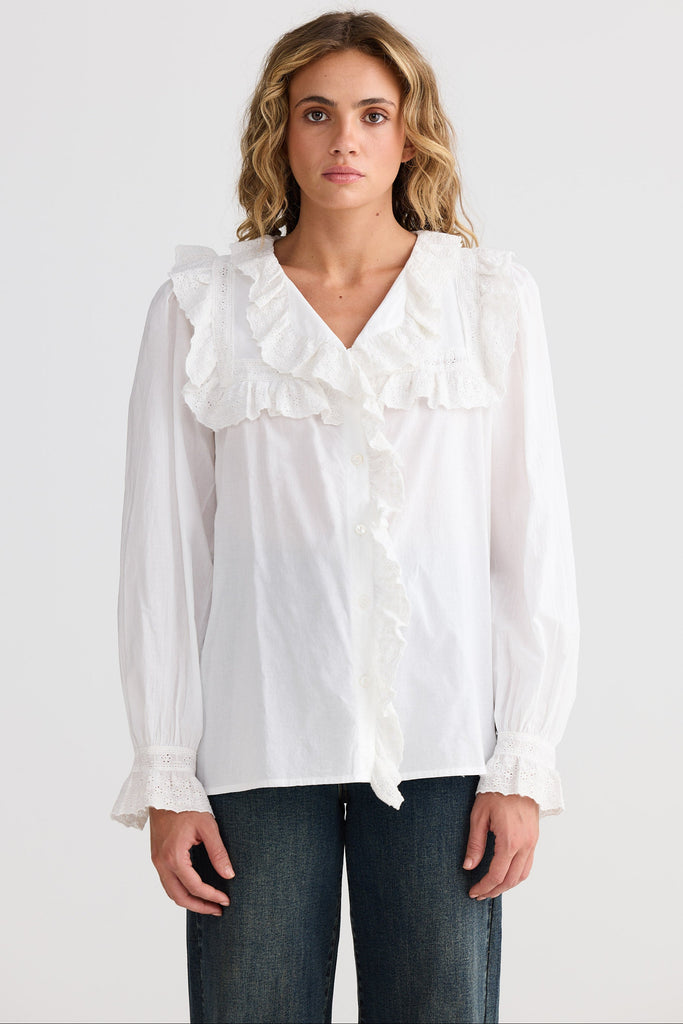 Woman wearing a white blouse with ruffled details on a plain background