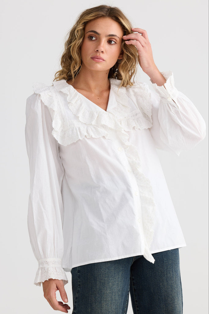 Woman wearing a white blouse and dark jeans on a plain background