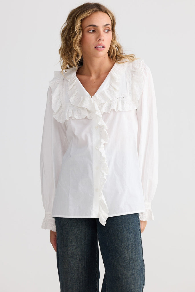 Woman wearing a white blouse with ruffles on a plain background