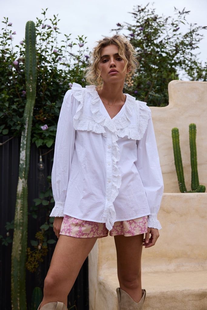 Woman wearing a white blouse and floral shorts standing in front of cacti.
