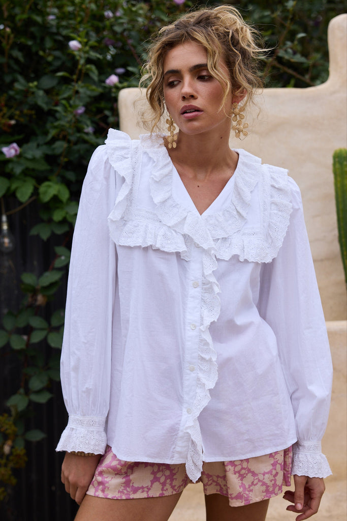 Woman wearing a white blouse with ruffled details and pink floral shorts outdoors.