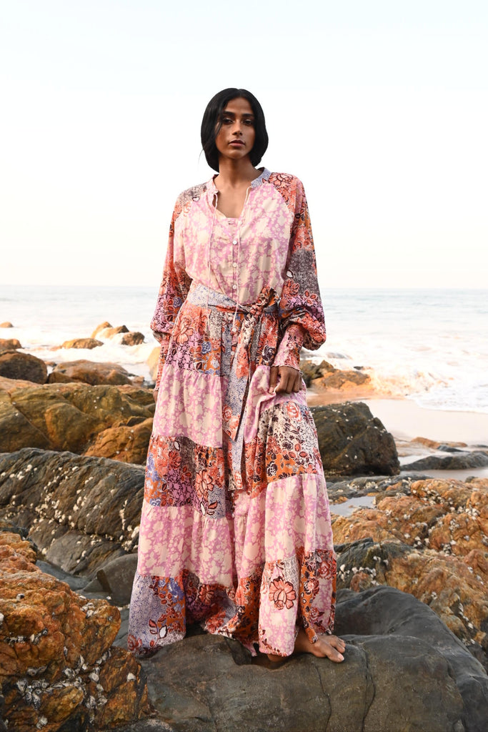 Woman in a floral dress standing on rocks at the beach.