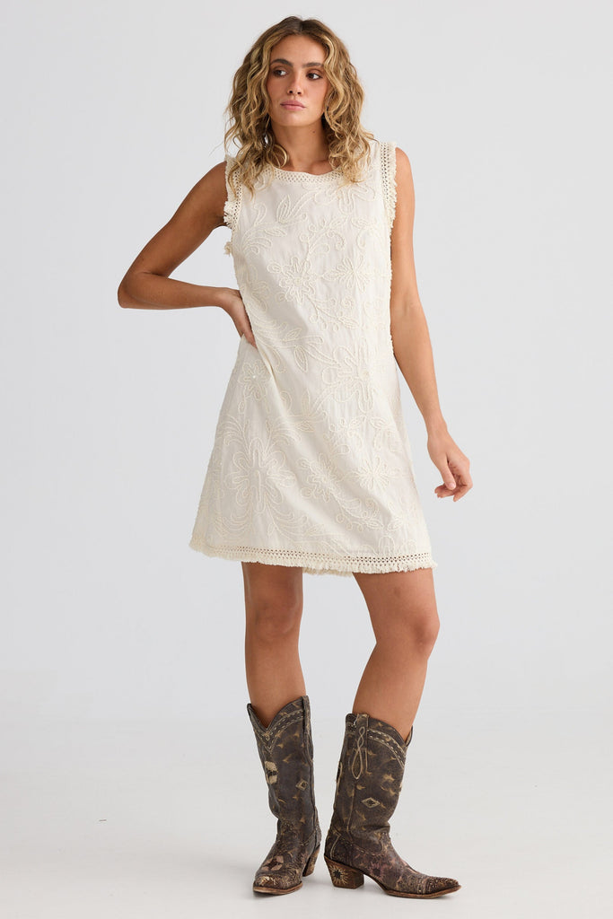 Woman wearing a white dress and brown boots on a plain background