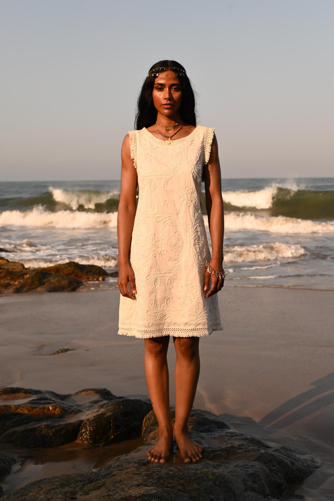 Woman in a cream embroidered dress standing on rocks on a beach