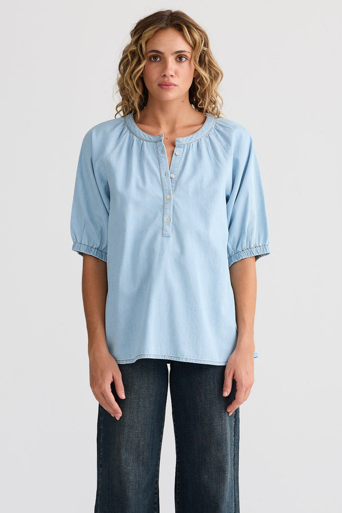 Woman wearing a light blue blouse and dark jeans on a white background