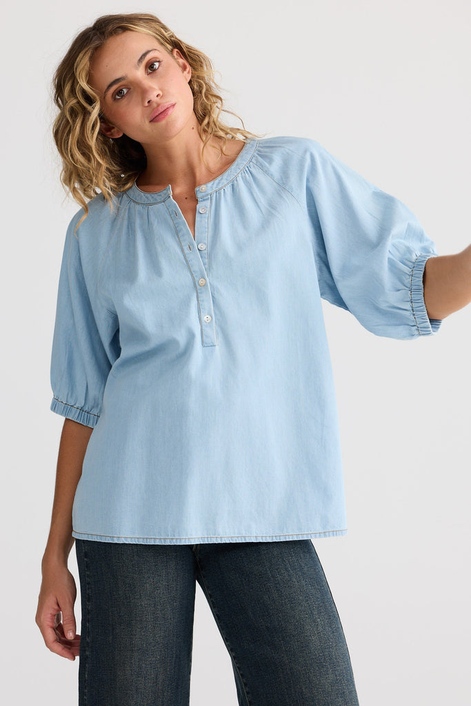 Woman wearing a light blue blouse with rolled-up sleeves against a white background