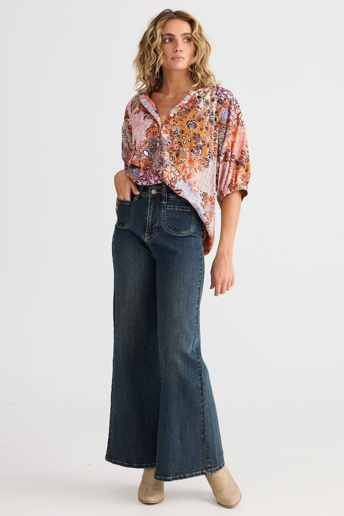 Woman wearing a patterned blouse and blue jeans on a white background