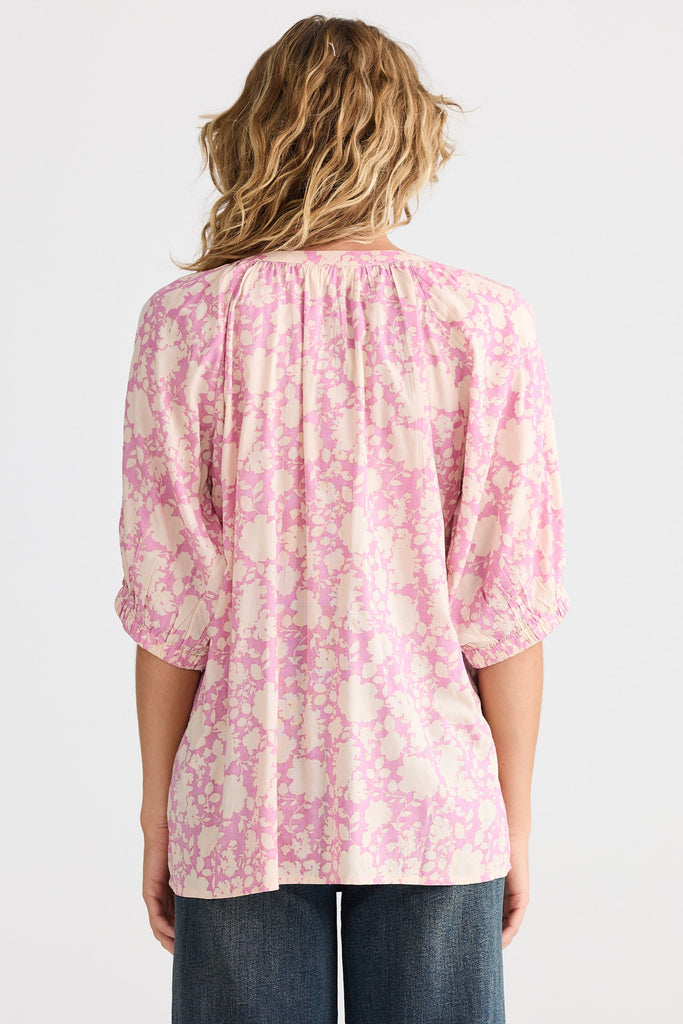Person wearing a pink floral blouse with blue jeans on a white background