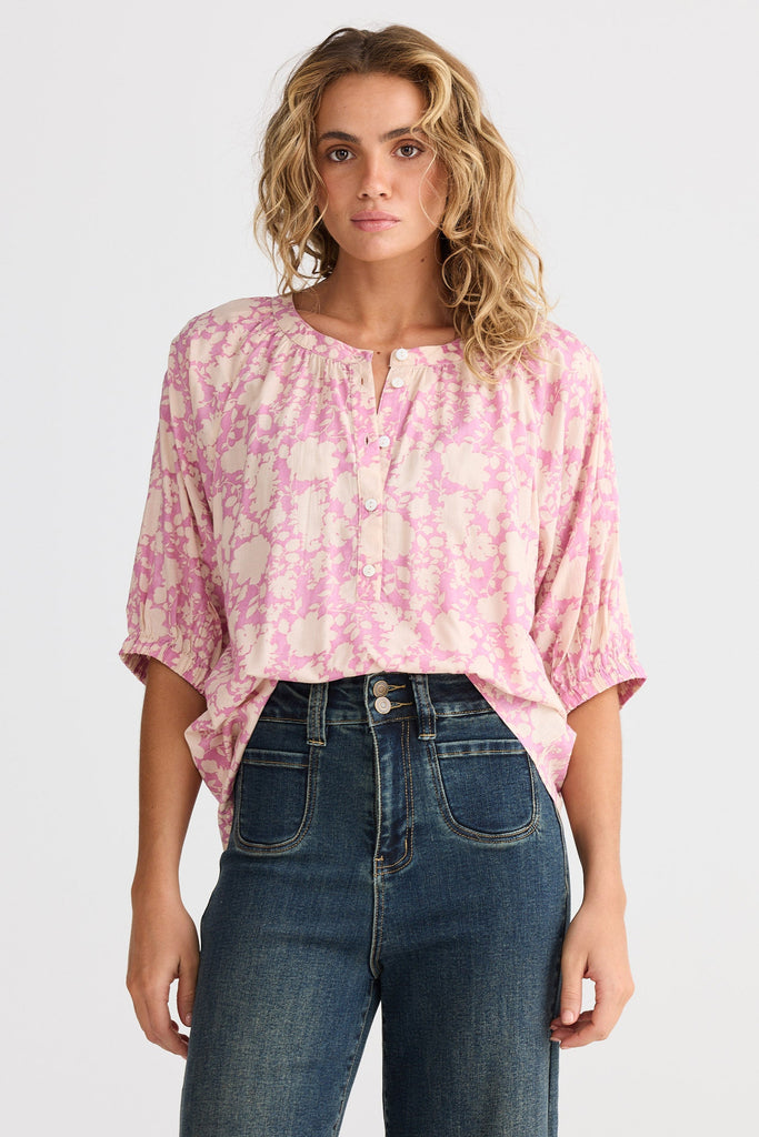 Woman wearing a pink floral blouse and blue jeans on a white background