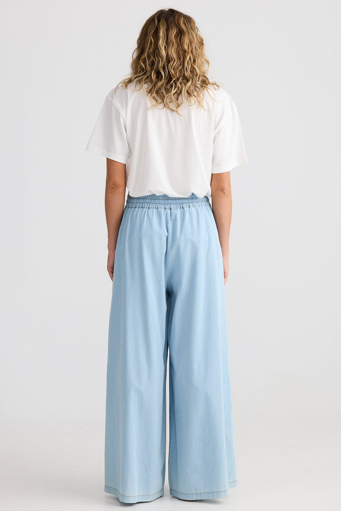Person wearing a white shirt and light blue wide-leg pants on a white background
