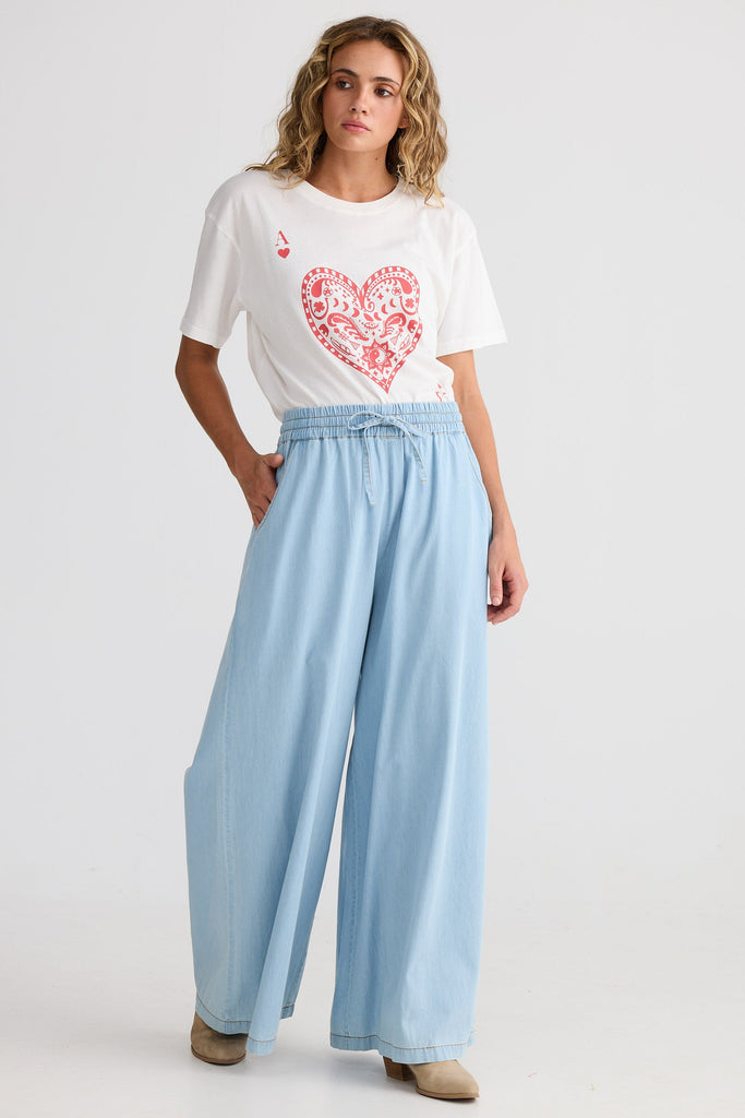 Woman wearing a white t-shirt with a red heart design and light blue pants on a white background