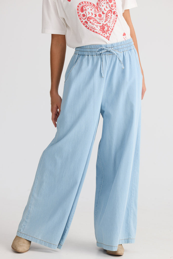 Person wearing light blue wide-leg jeans and a white t-shirt with a red heart design on a plain background