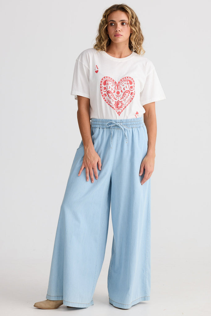 Woman wearing a white t-shirt with a red heart design and light blue wide-leg pants on a white background