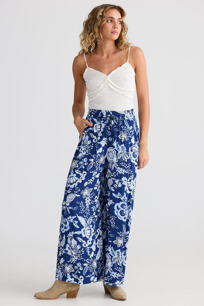 Woman wearing a white top and blue floral pants on a white background