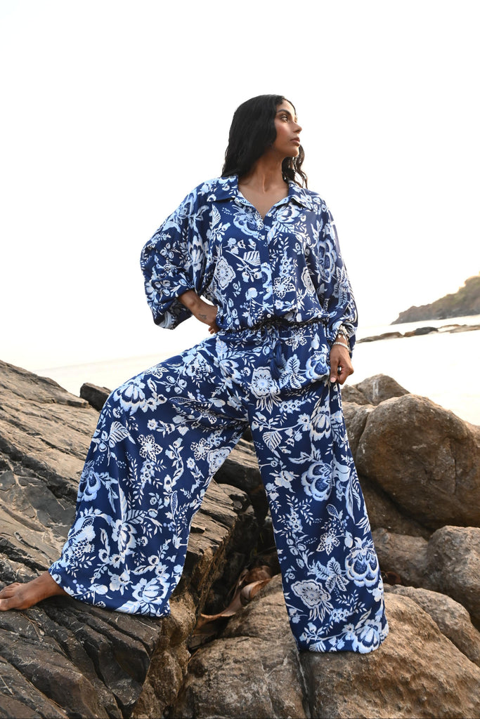 Person wearing a blue floral outfit standing on rocks with a scenic background