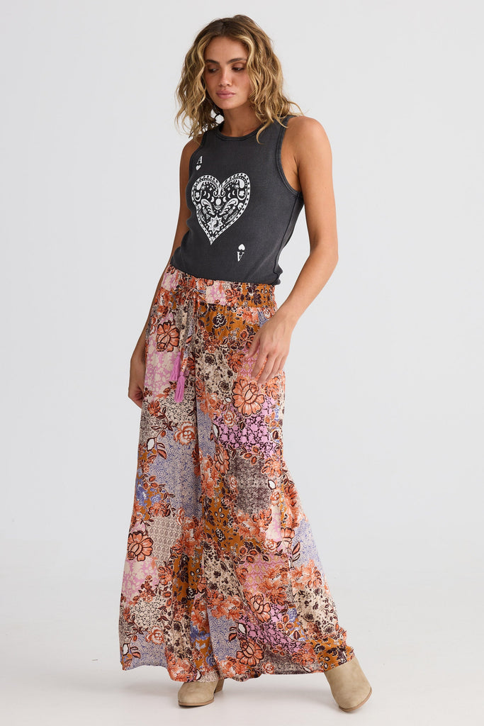 Woman wearing a black sleeveless top with a heart design and long, colorful floral pant on a white background