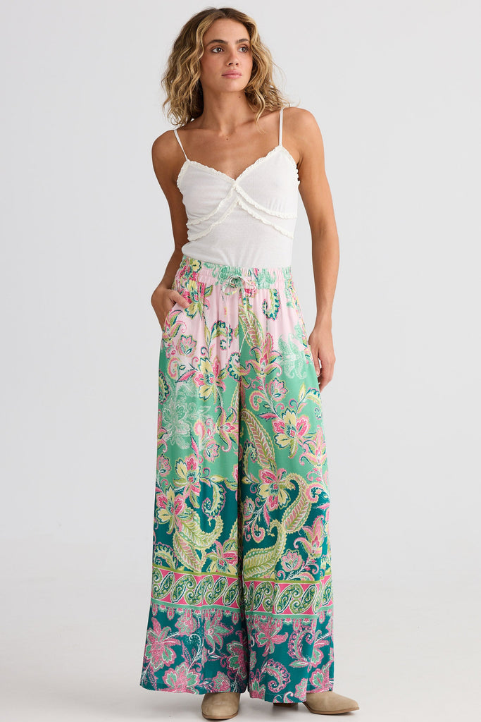 Woman wearing a white top and colorful patterned pants on a white background