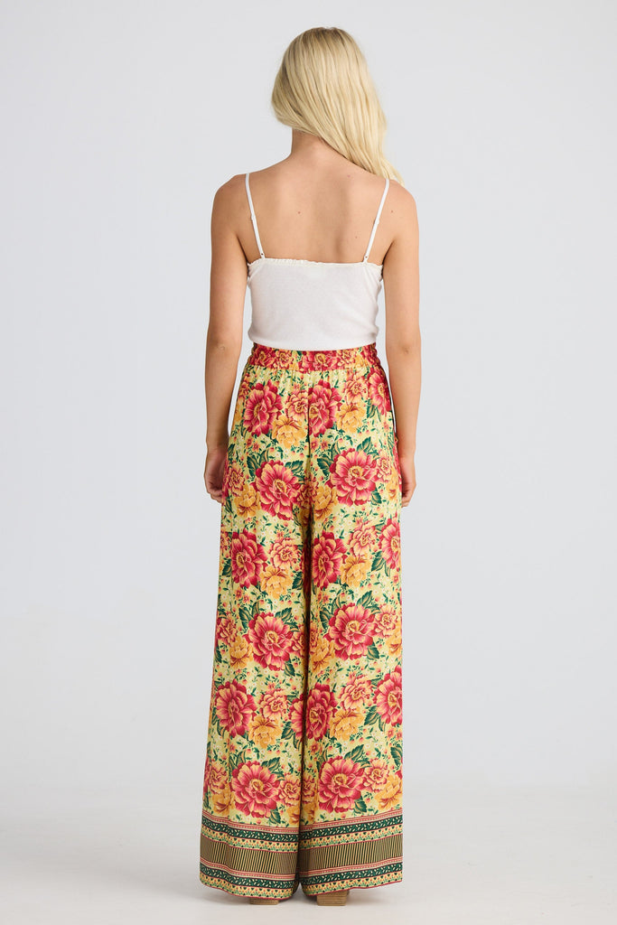 Woman wearing a white top and colorful floral pants on a white background