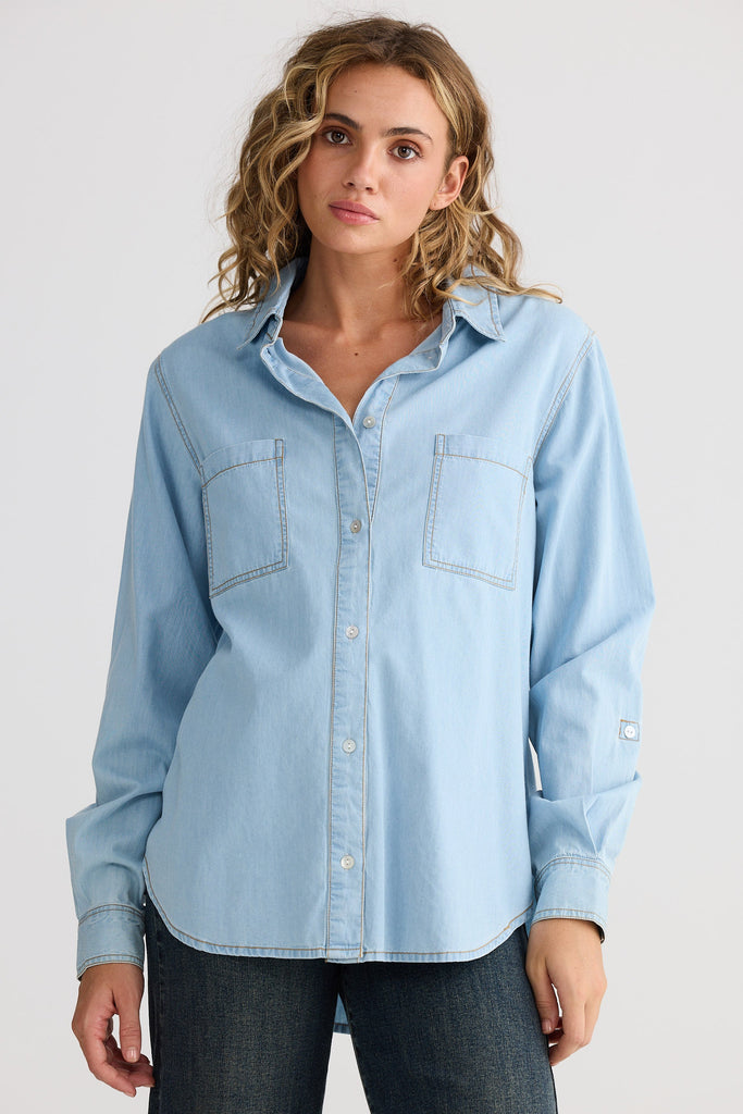 Woman wearing a light blue denim shirt against a white background