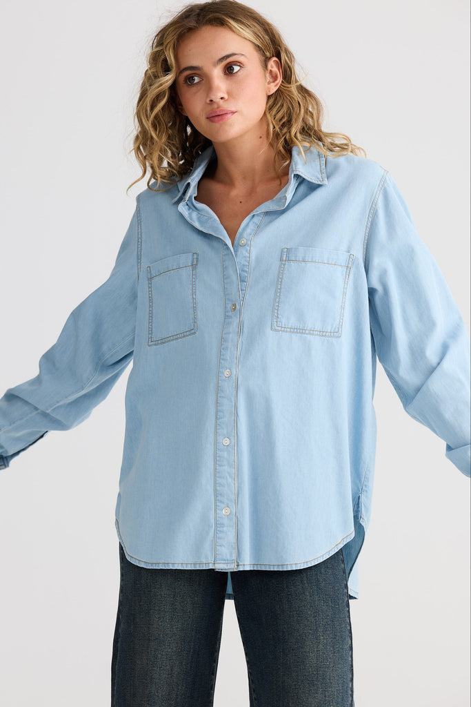 Woman wearing a light blue denim shirt against a plain background