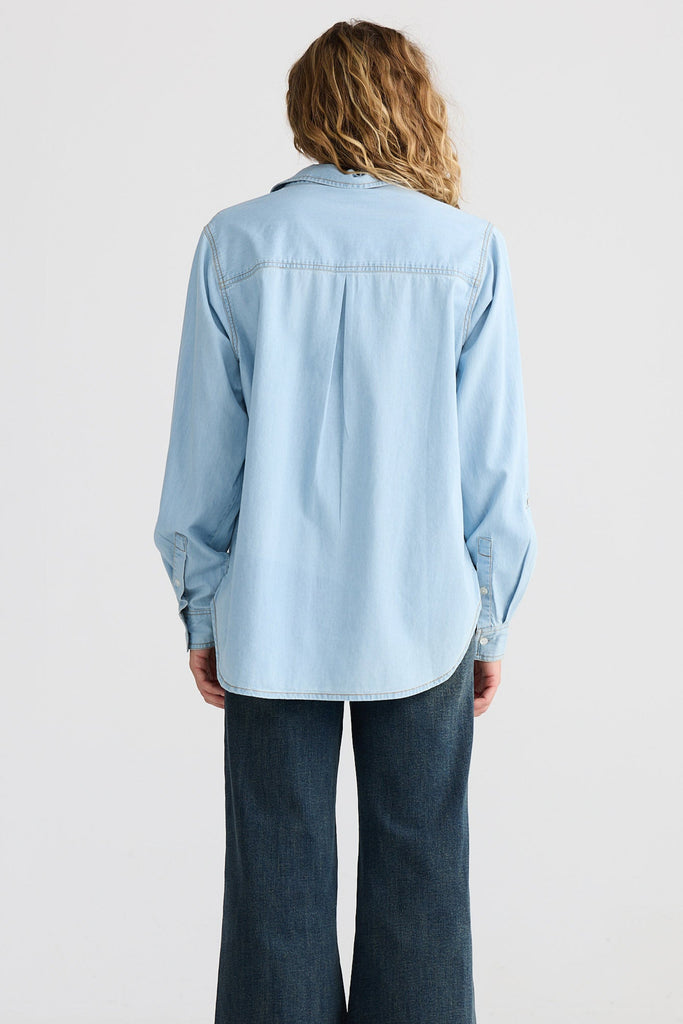 Person wearing a light blue denim shirt and dark blue jeans on a white background
