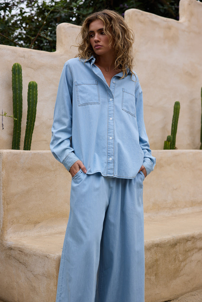 Woman wearing a light blue outfit standing in front of a beige wall with cacti.
