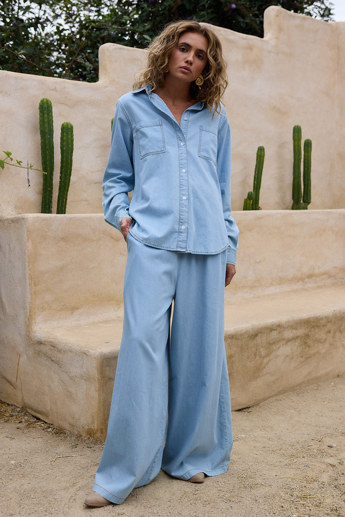 Woman in a light blue outfit standing in front of a stone wall with cacti.