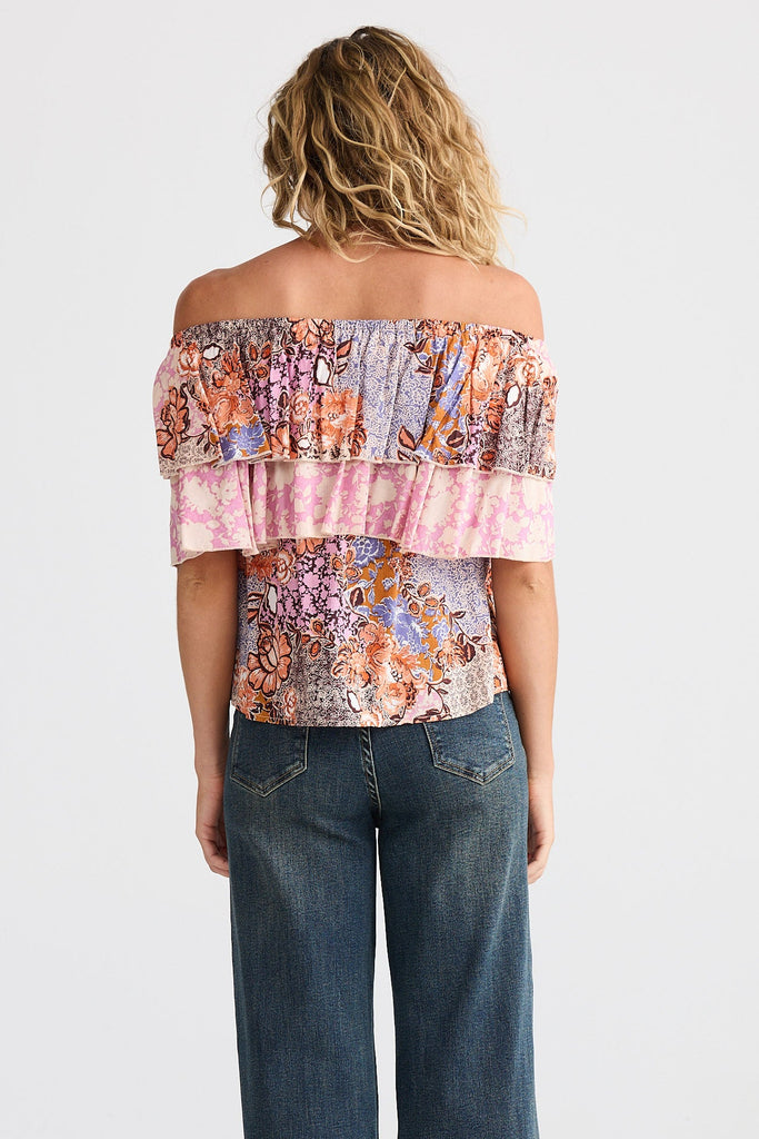 Person wearing a colorful off-shoulder top and blue jeans on a white background