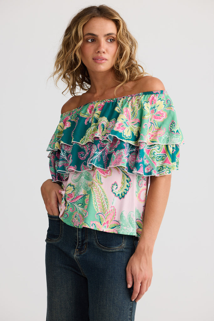 Woman wearing a colorful off-shoulder top with floral patterns on a white background
