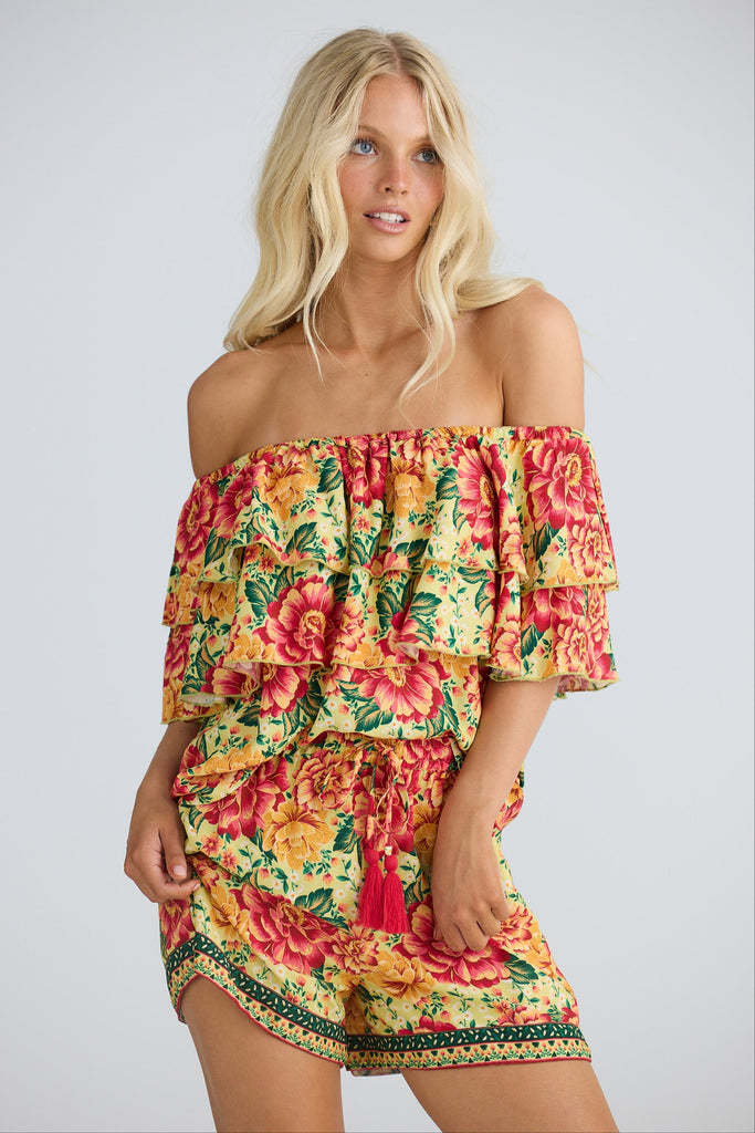 Woman wearing a colorful floral off-shoulder top and matching shorts on a plain background