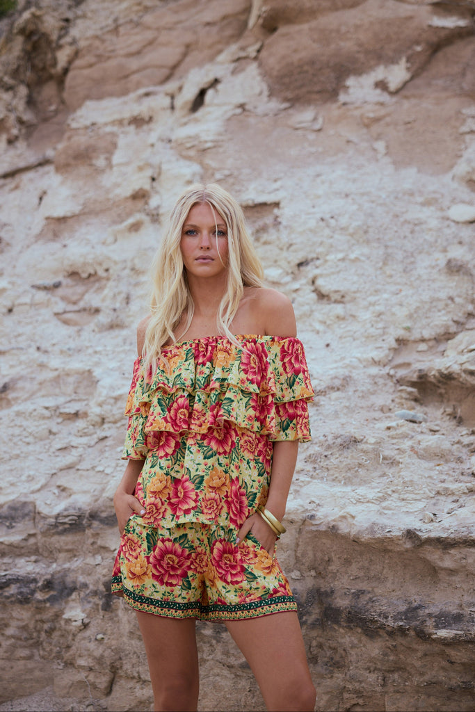 Woman in a floral off-shoulder top and matching shorts standing against a rocky wall.