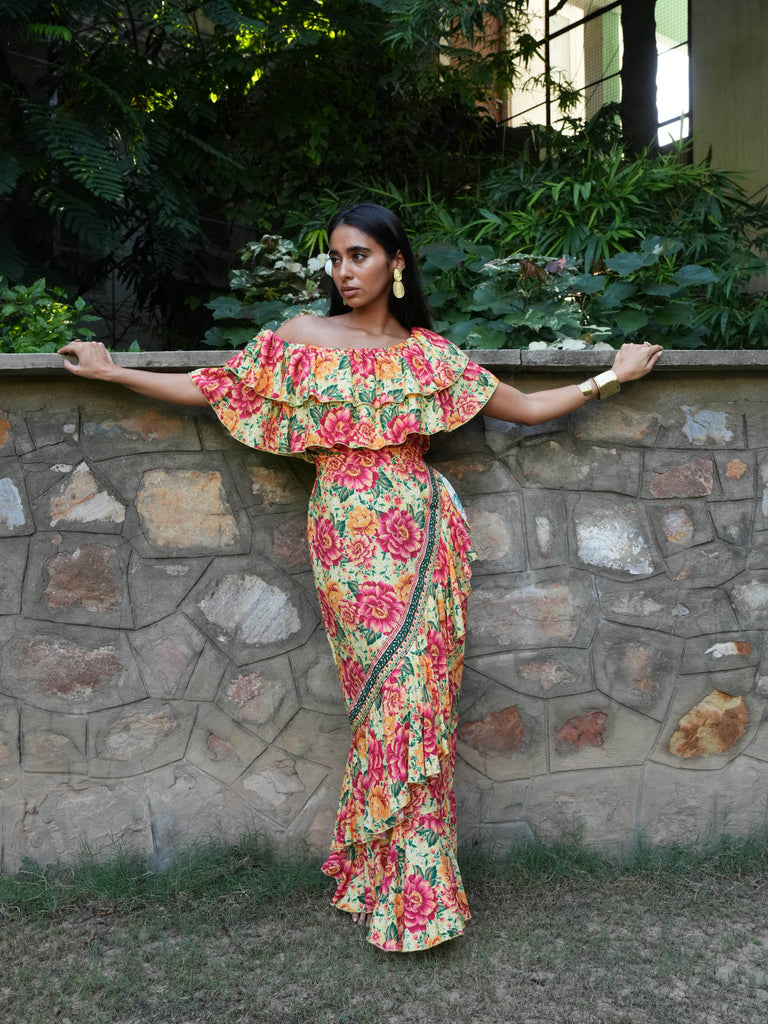 Woman in a floral off the shoulder dress and matching skirt standing against a stone wall with greenery in the background